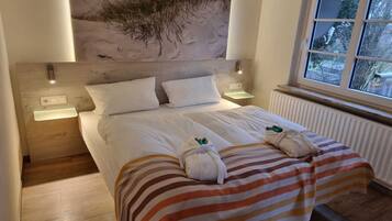 Een netjes opgemaakt bed met gestreept beddengoed, een hoofdbord met natuurkunst, nachtlampjes en een raam met uitzicht op groen.