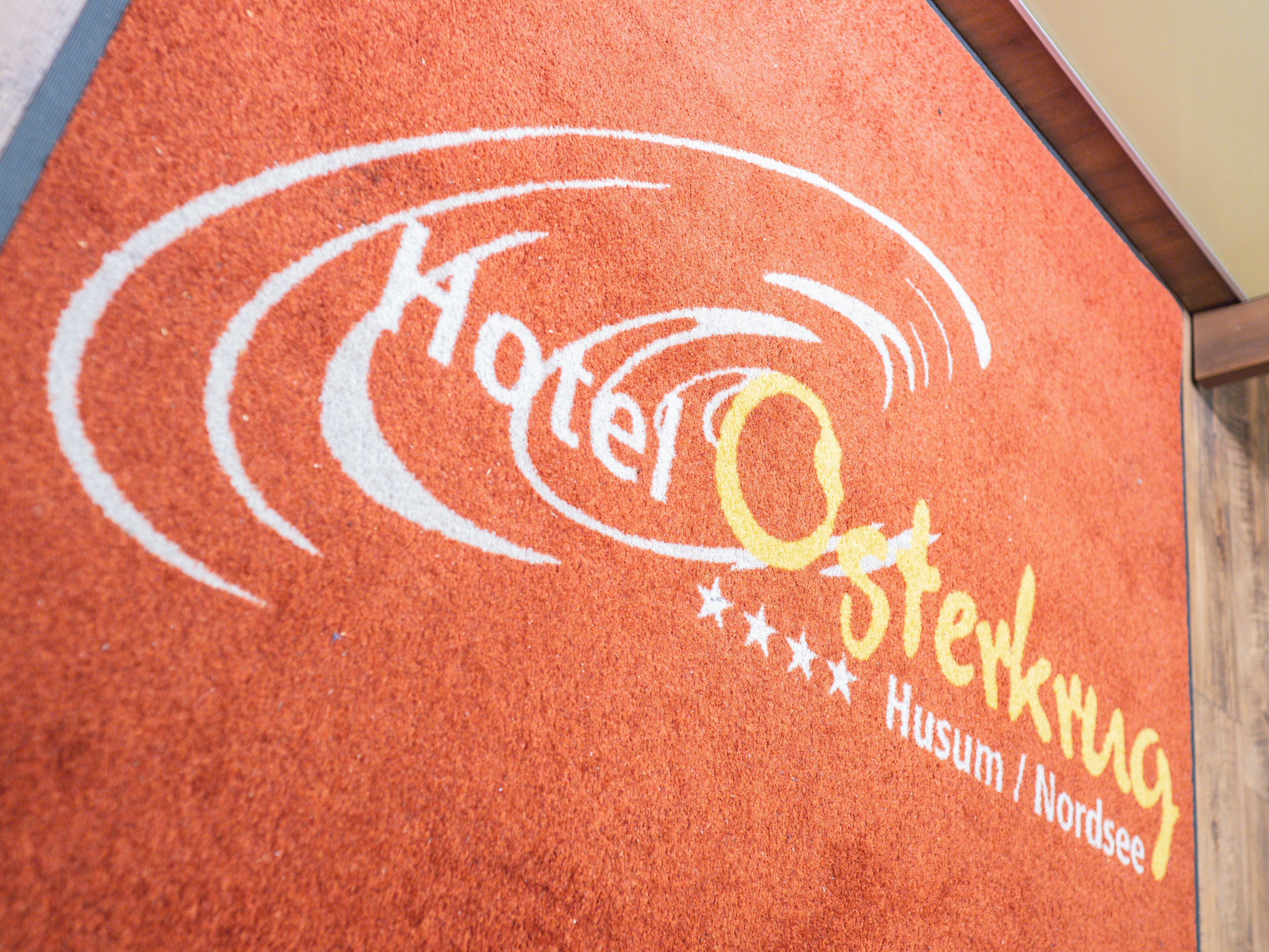 Primer plano de una superficie roja con textura, que muestra un logotipo y el texto "Hotel O St. Kjerring Husum / Nordsee".