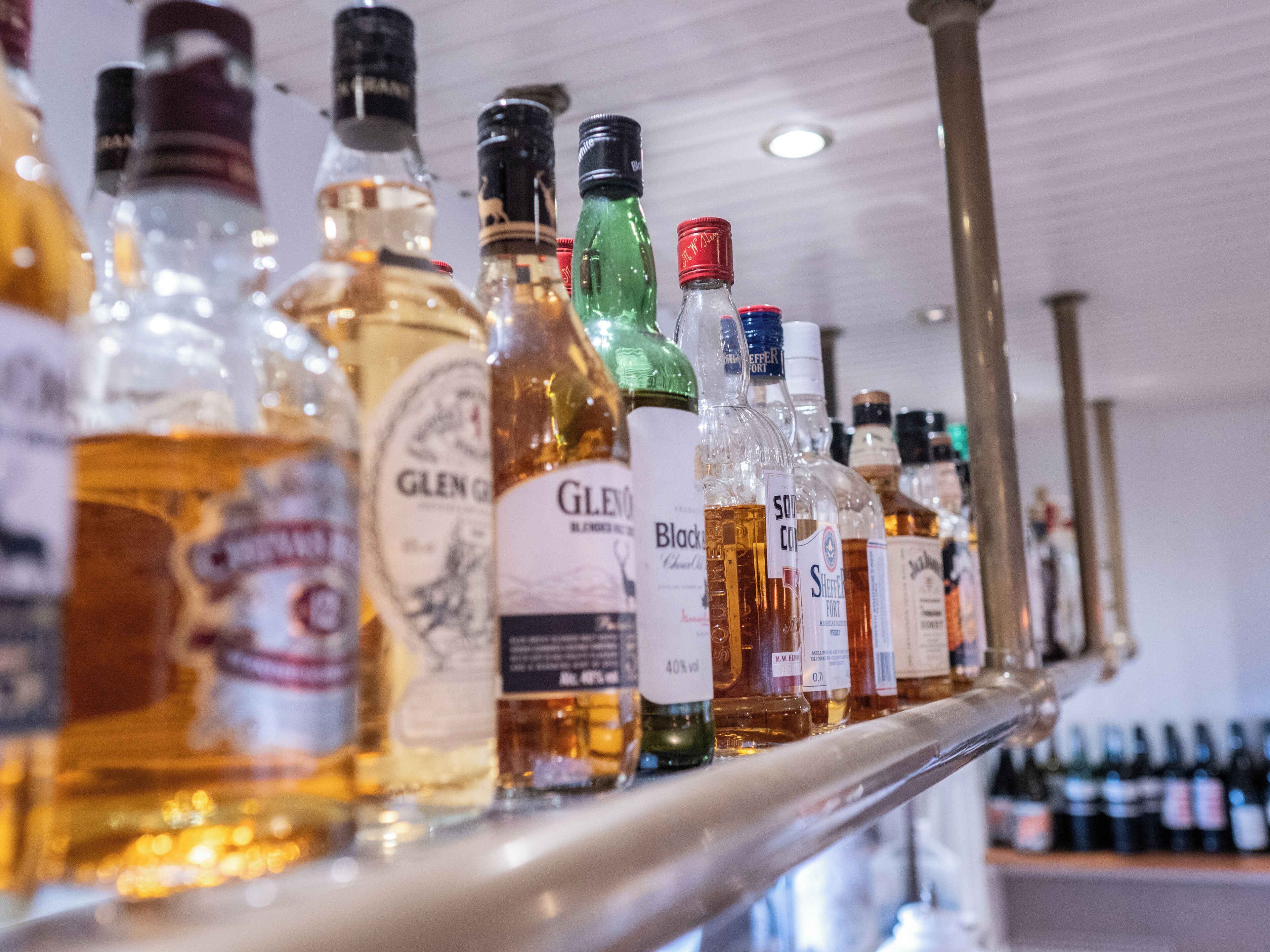 A variety of liquor bottles on a shelf in a bar setting.