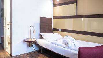 A modern hotel room with a wooden floor, a bed with white bedding, a bedside table with a lamp, and a red chair.