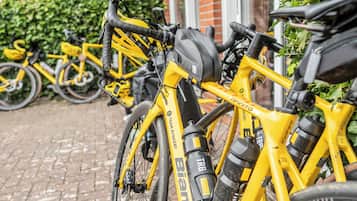A row of yellow bicycles parked in an outdoor area with a brick wall and greenery in the background.