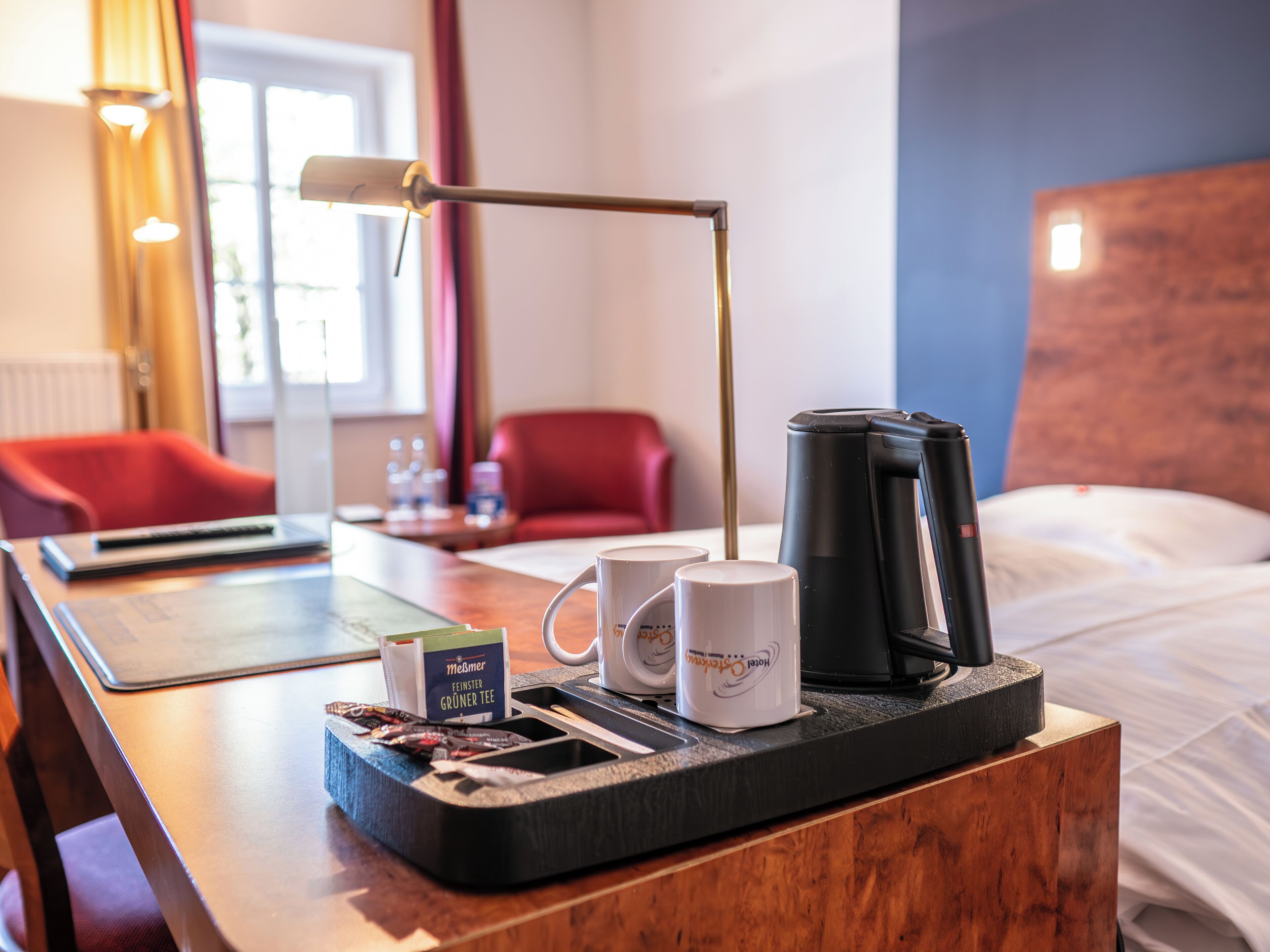 Een hotelkamer met een houten nachtkastje, een dienblad met een koffiezetapparaat, twee mokken en een theeblik.