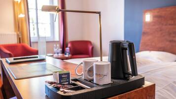 Een hotelkamer met een houten nachtkastje, een dienblad met een koffiezetapparaat, twee mokken en een theeblik.