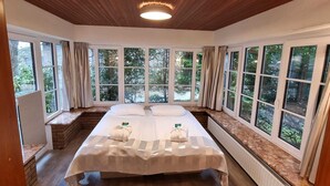 Un dormitorio con una cama grande, techo de madera y varias ventanas que dan a zonas verdes.