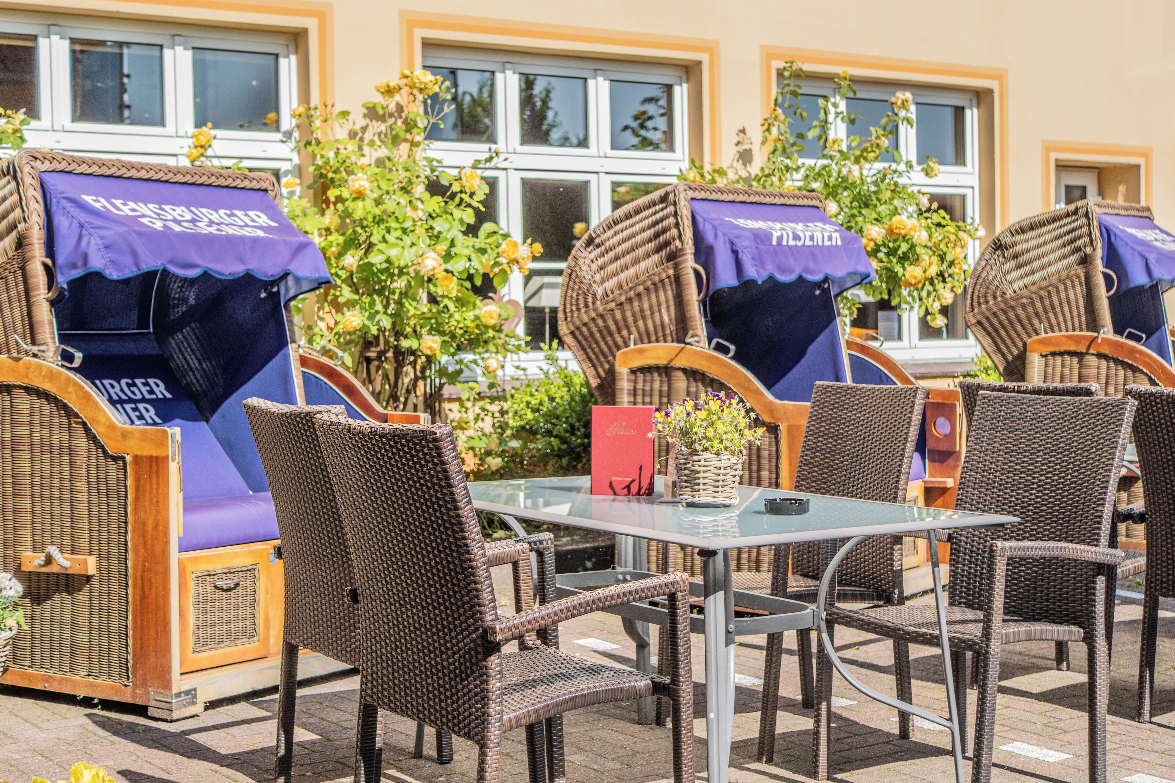 Mobilier d’extérieur en osier, avec des auvents violets, une table en verre et une enseigne rouge.