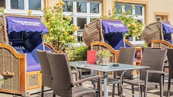 Mobilier d’extérieur en osier, avec des auvents violets, une table en verre et une enseigne rouge.