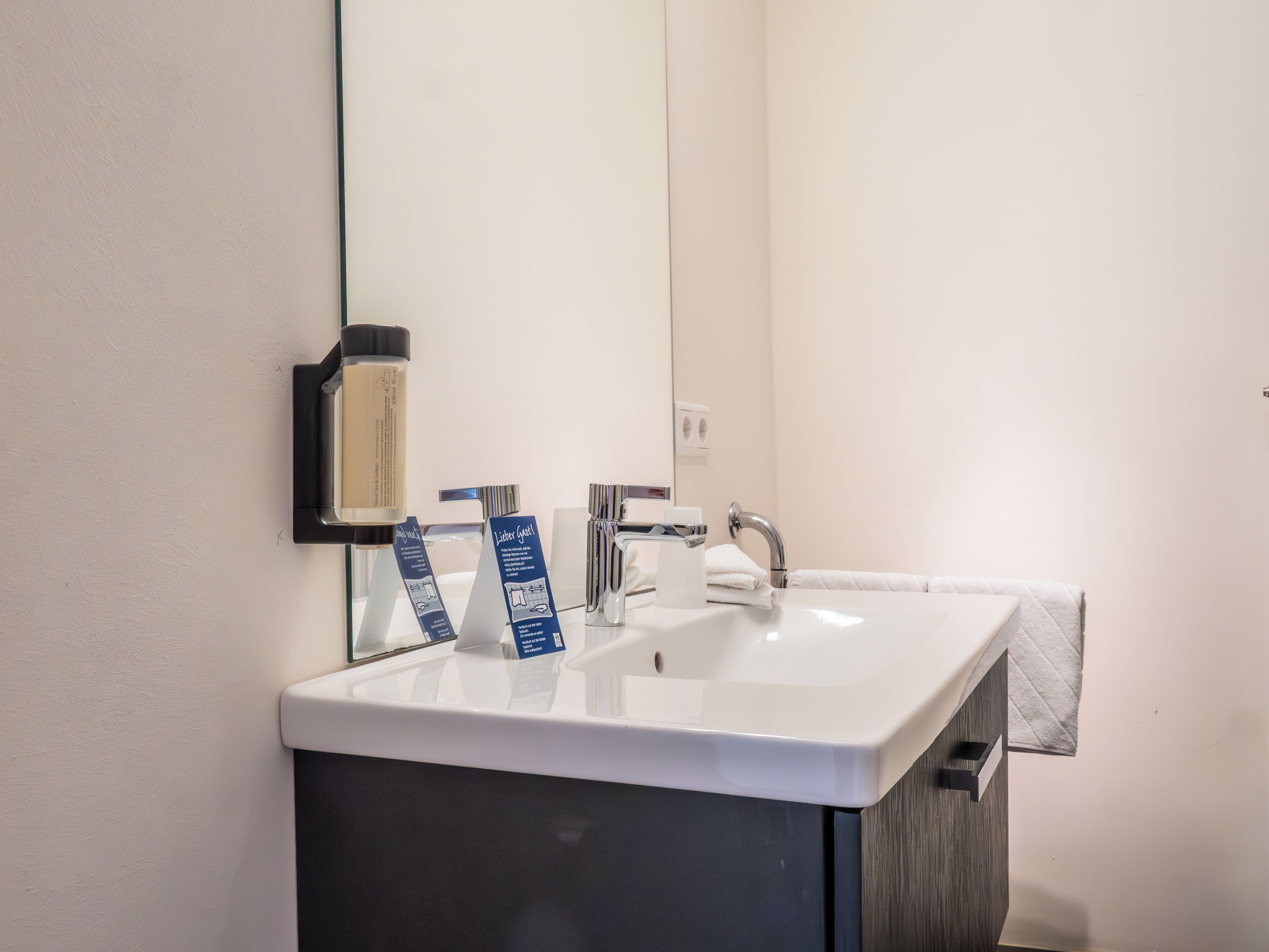 Un bagno moderno con un lavandino bianco, uno specchio grande e un mobile contenitore scuro.