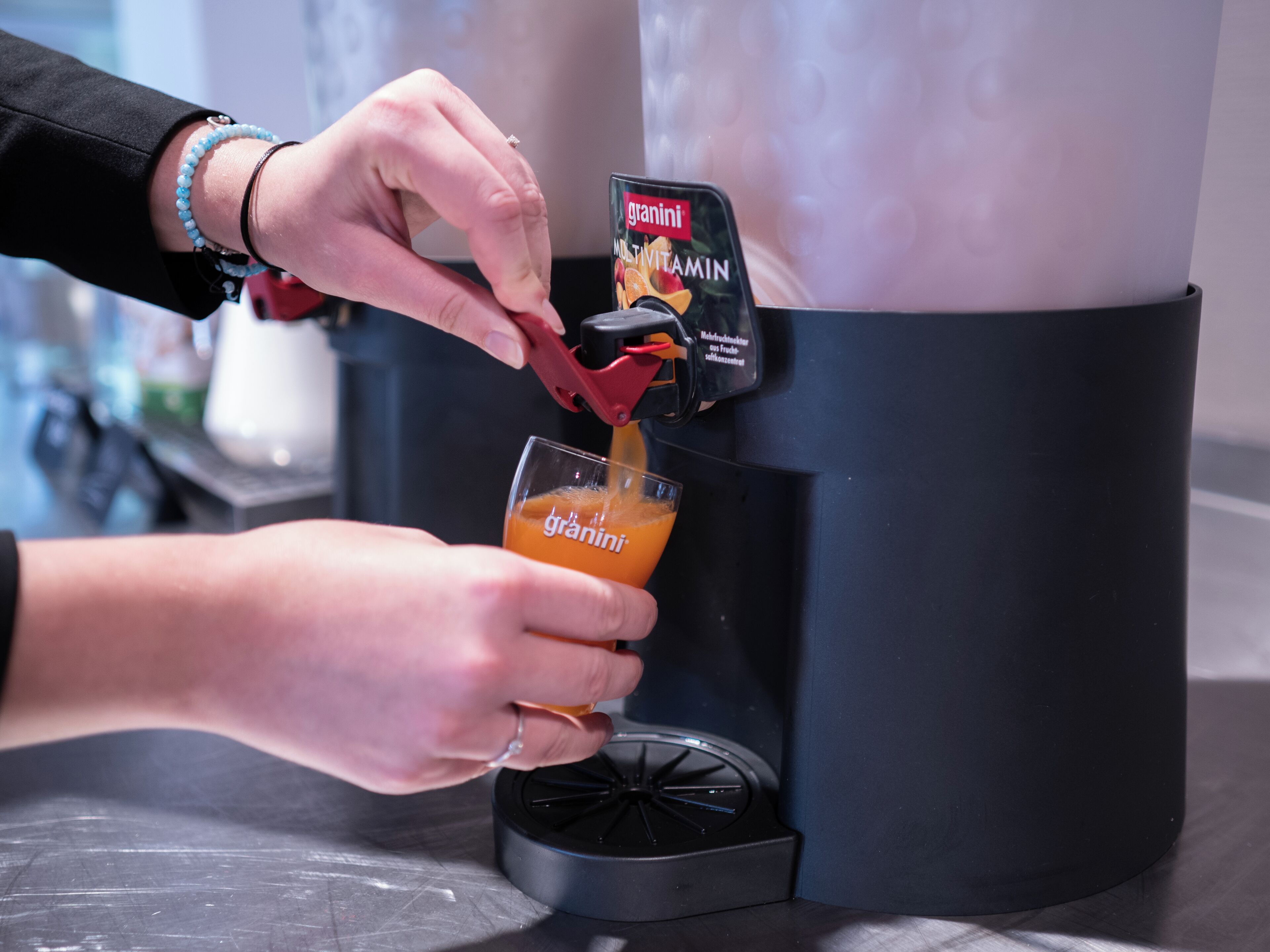 A person pouring orange juice from a dispenser into a glass.