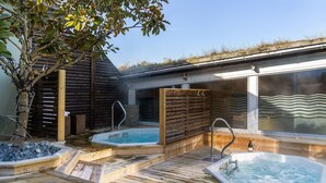 Une terrasse en bois avec deux bains à remous, un arbre et un espace clos par des baies vitrées offrant une vue panoramique.