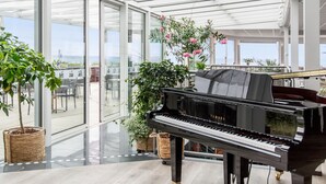 Un piano à queue dans une pièce spacieuse et bien éclairée, dotée de grandes fenêtres en verre et agrémentée de plantes en pot.