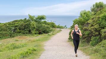 A person jogging on a gravel path surrounded by greenery and overlooking a body of water.