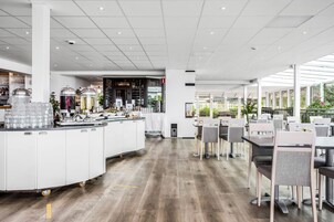 A modern restaurant with a central bar area, white cabinetry, and a wooden floor.