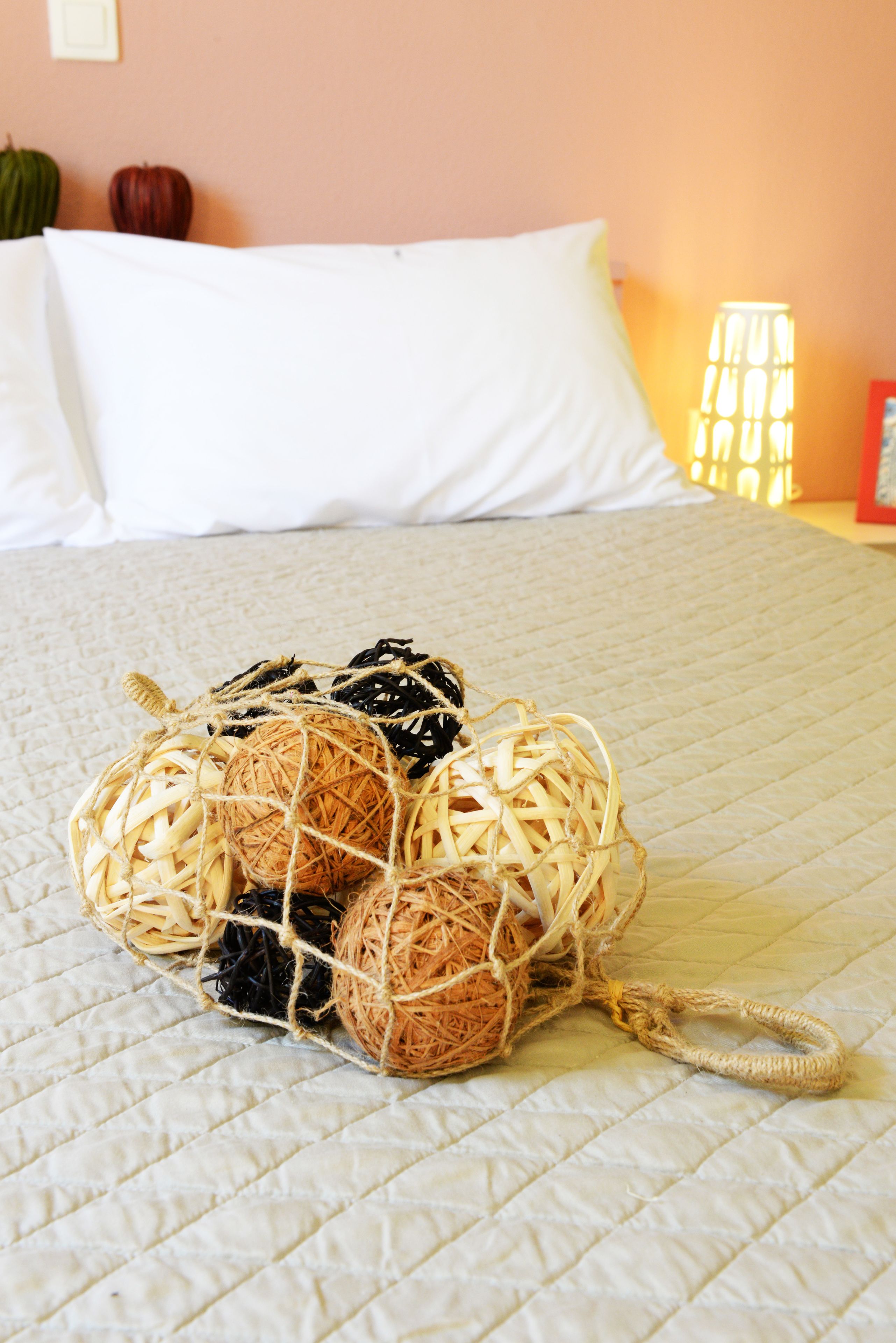 A bed with a white quilted bedspread, a wicker basket with balls of yarn, and a bedside lamp.