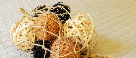A bed with a white quilted bedspread, a wicker basket with balls of yarn, and a bedside lamp.