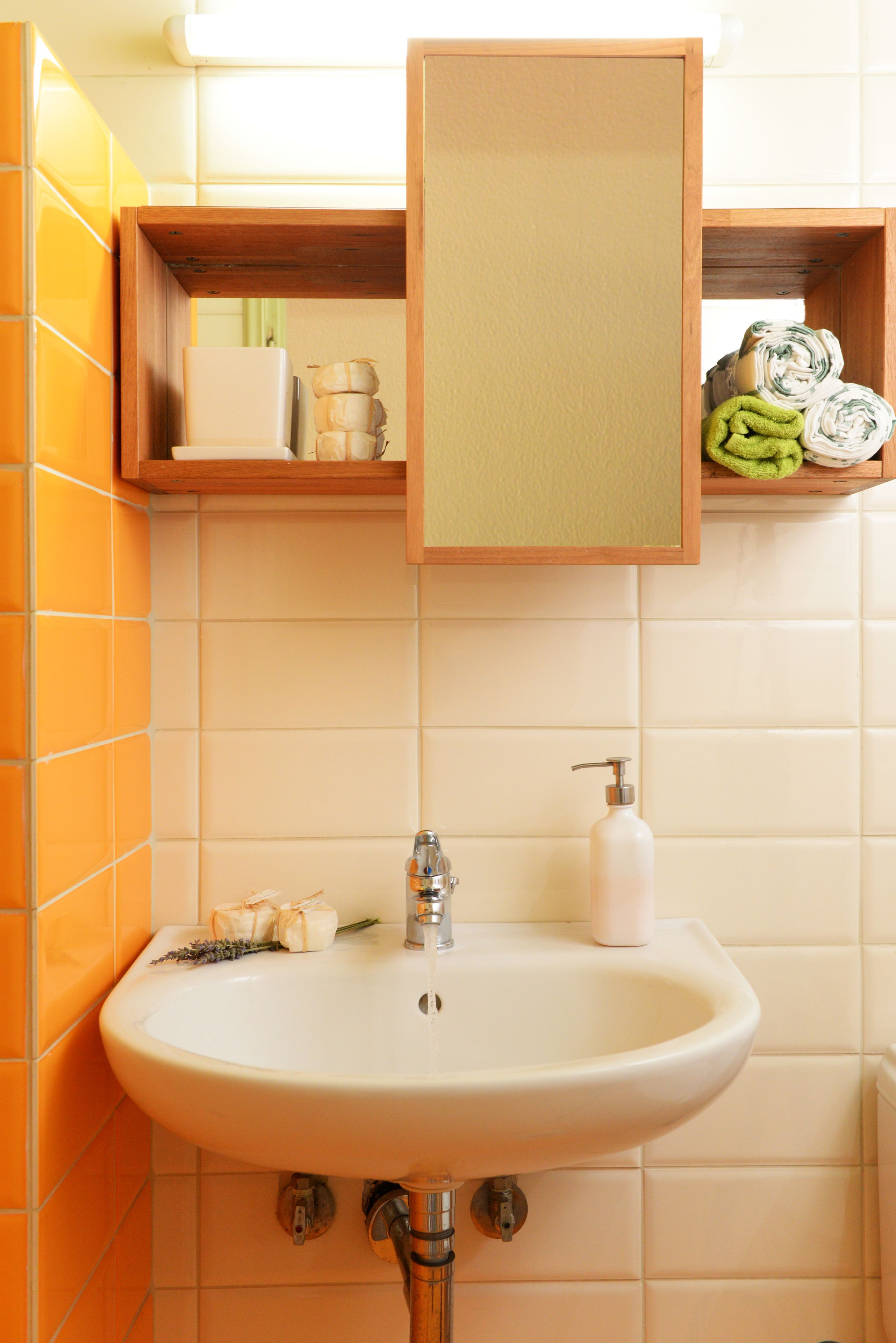 A bathroom with a white sink, a mirror, and a shelf above the sink holding toiletries.