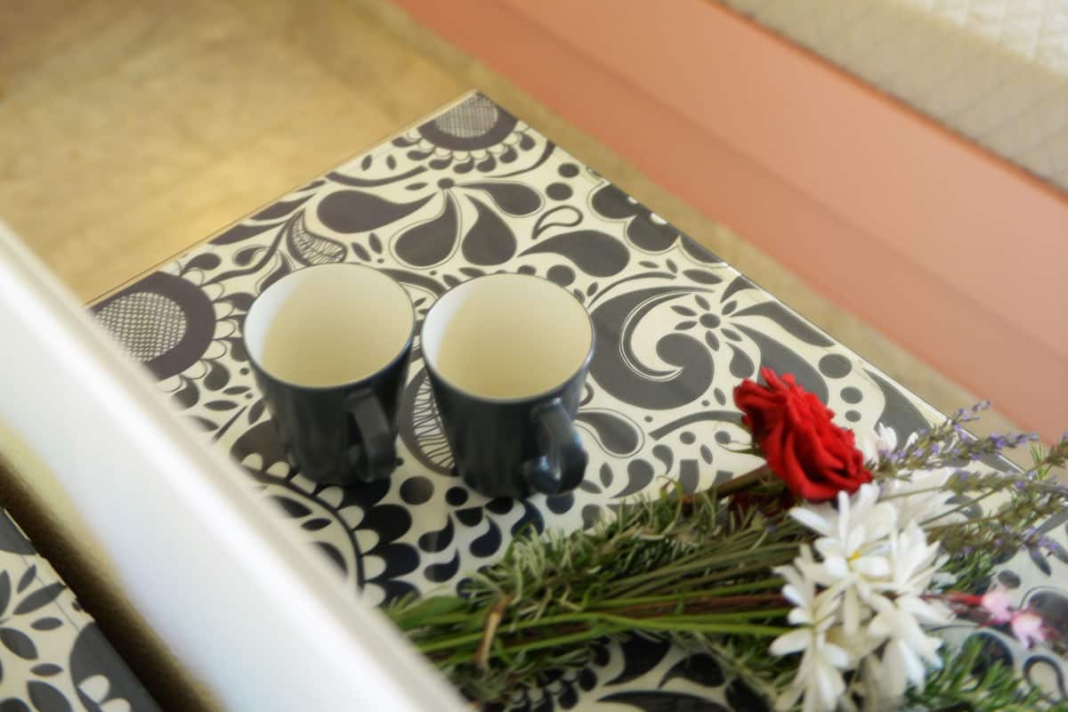 A neatly arranged bedroom with a bed, bedside table, and a decorative table with a vase of flowers and two cups.