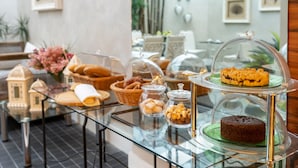 Un bufé de desayuno con diversos pasteles, pan y un pastel expuestos en un mostrador de vidrio.