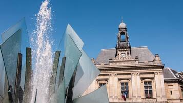 Un bâtiment historique doté d’une tour horlogée et d’une fontaine ornée de sculptures géométriques.