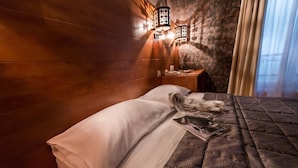 Habitación de hotel con pared de madera, cama con ropa blanca y mesita de noche con lámpara.