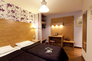 A hotel room with a bed, bedside table, desk, chair, and a small stool. - Palma Hotel (Paris)
