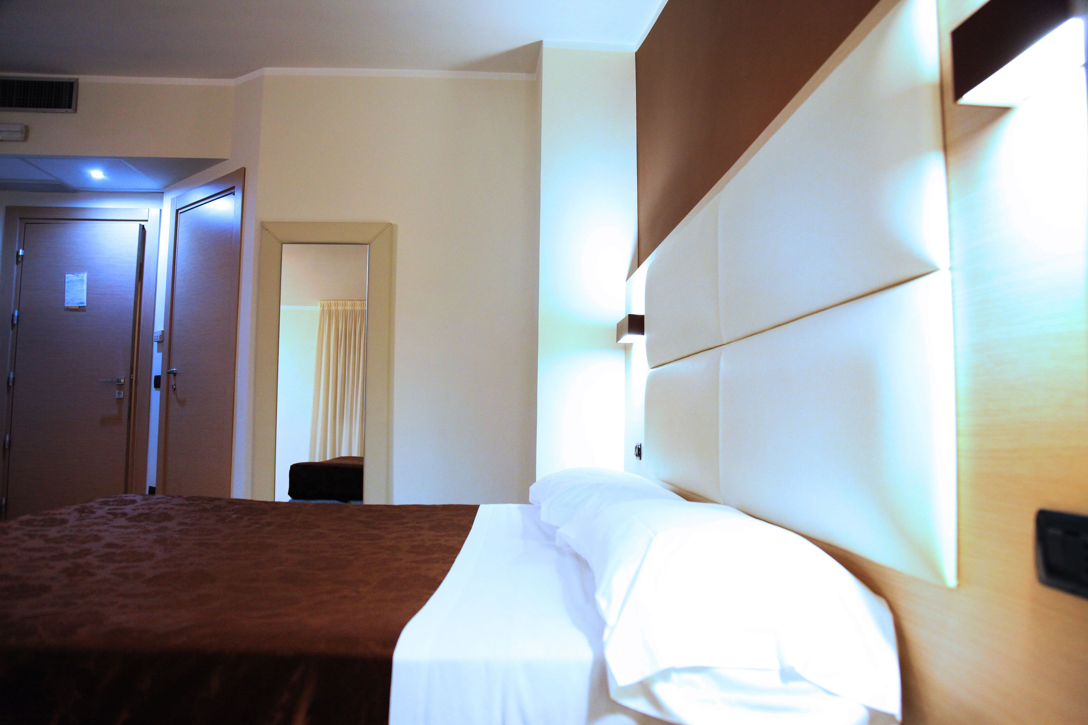 Una camera d'albergo con un letto, una porta e una lampada fissata al muro.