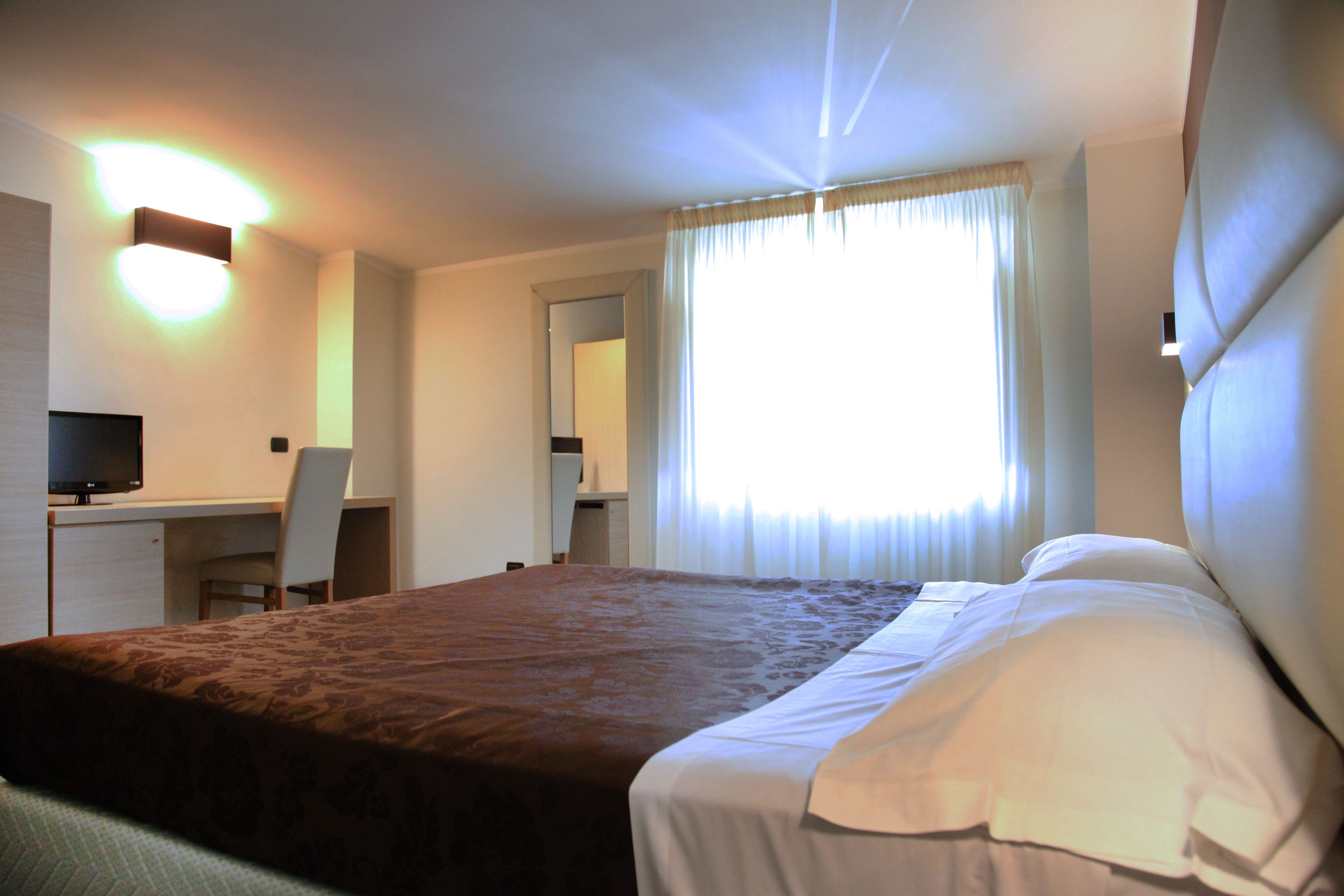 Una habitación de hotel con cama, escritorio, silla y televisor.