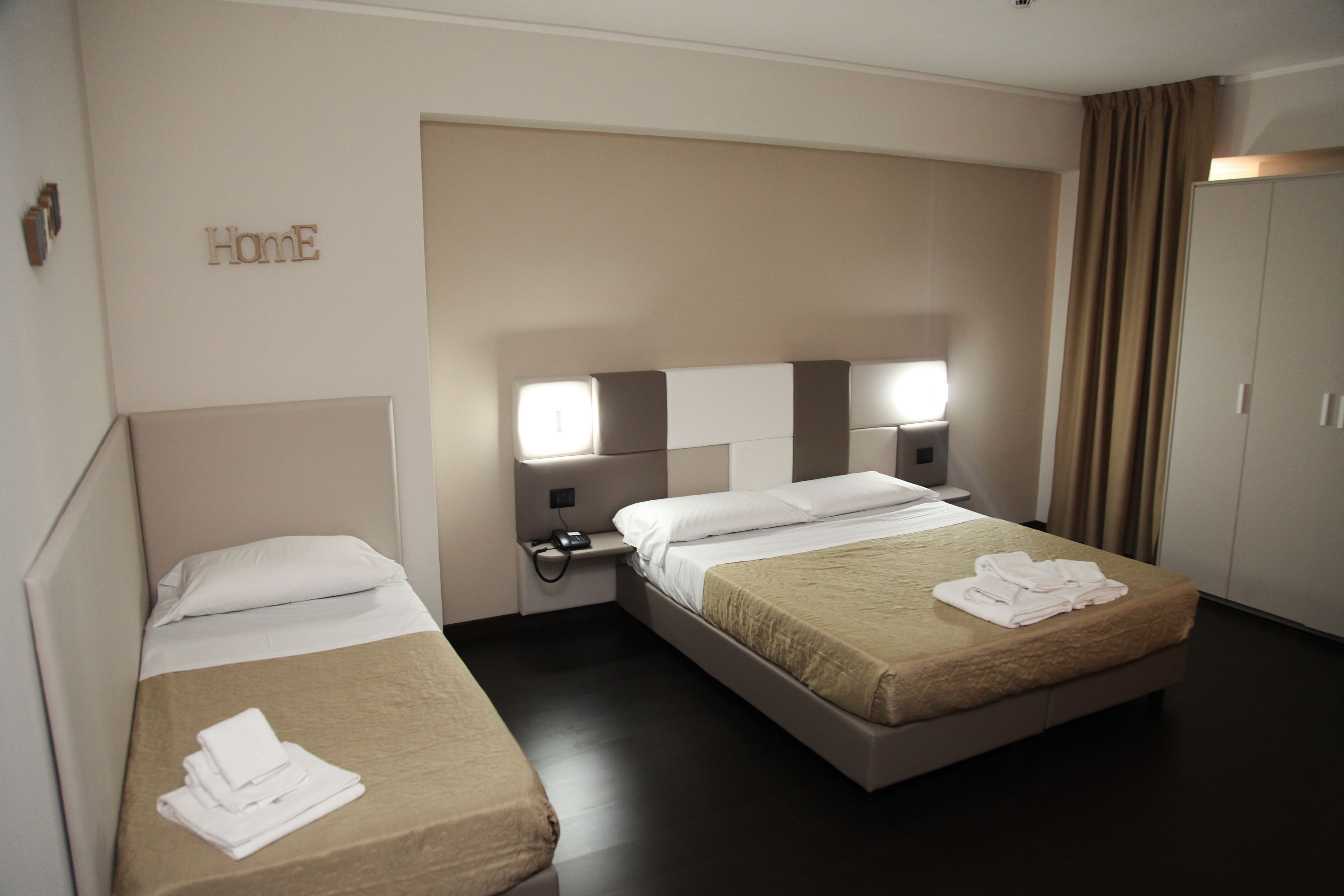 A hotel room with two beds, a wardrobe, and a "Home" sign on the wall.
