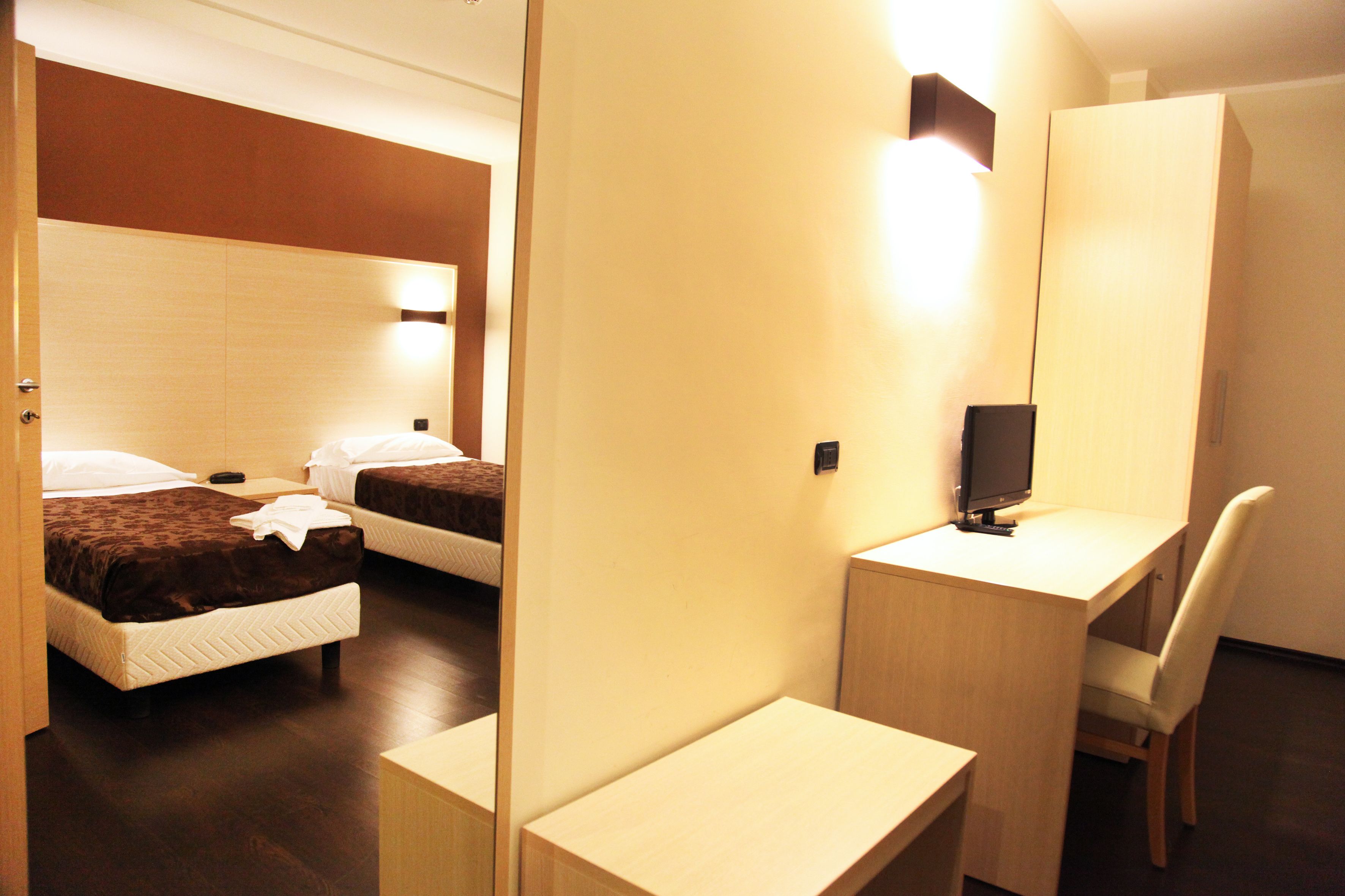 A hotel room with two beds, a desk, a chair, and a television.
