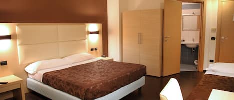 Habitación de hotel con una cama grande, mesitas de noche, armario, baño con espejo y lavabo, y una silla.