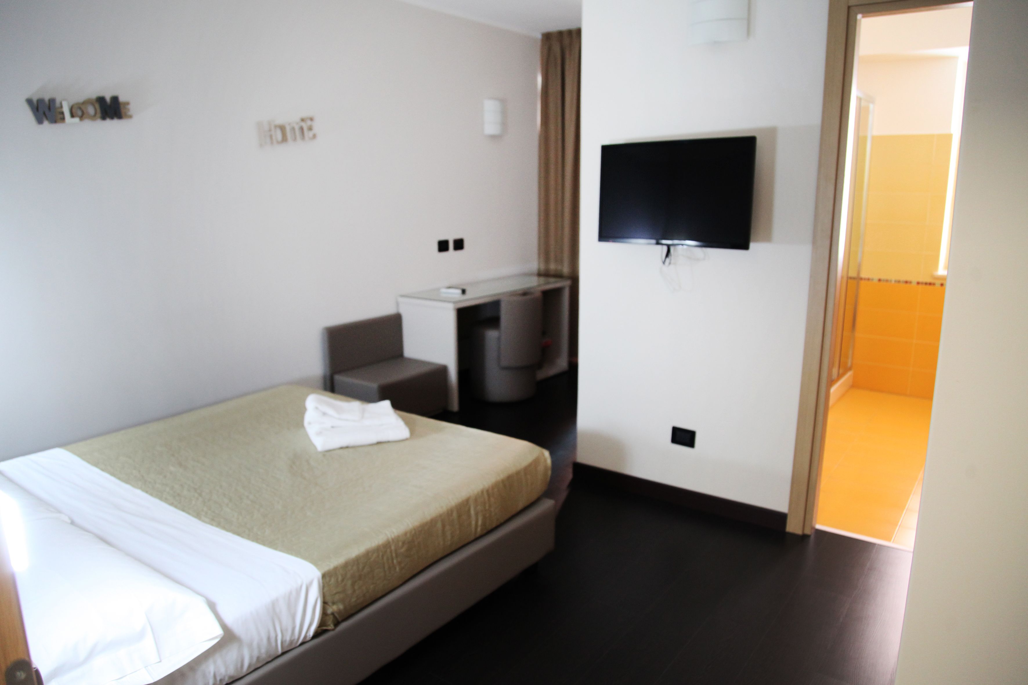 A hotel room with a bed, a desk, a TV, and a bathroom visible through an open door.
