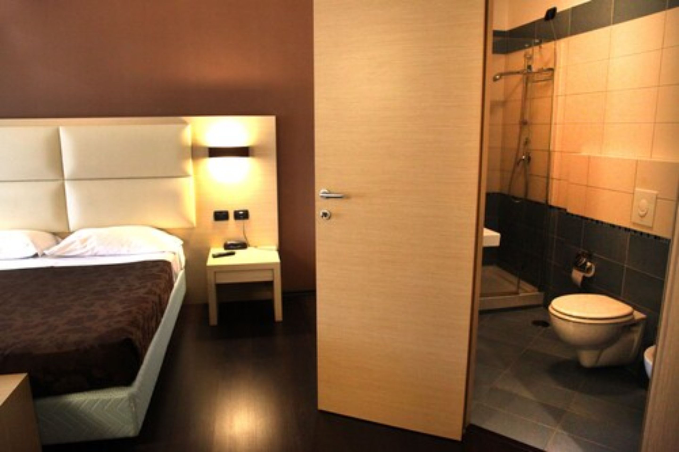 Ein Hotelzimmer mit Bett, Nachttisch und einem Badezimmer mit Dusche, Toilette und Waschbecken.