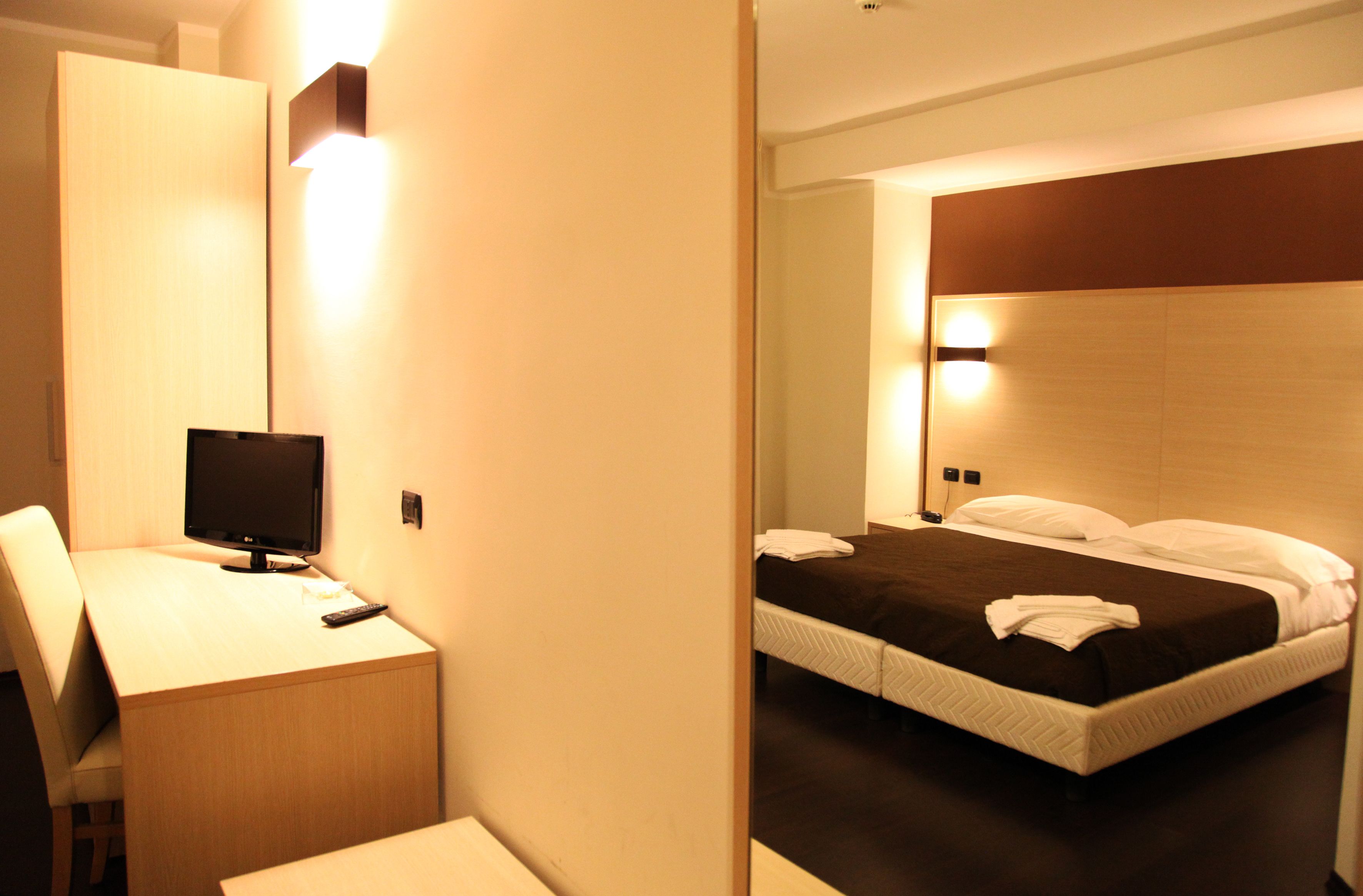 Una habitación de hotel con escritorio, cama con ropa blanca y espejo.