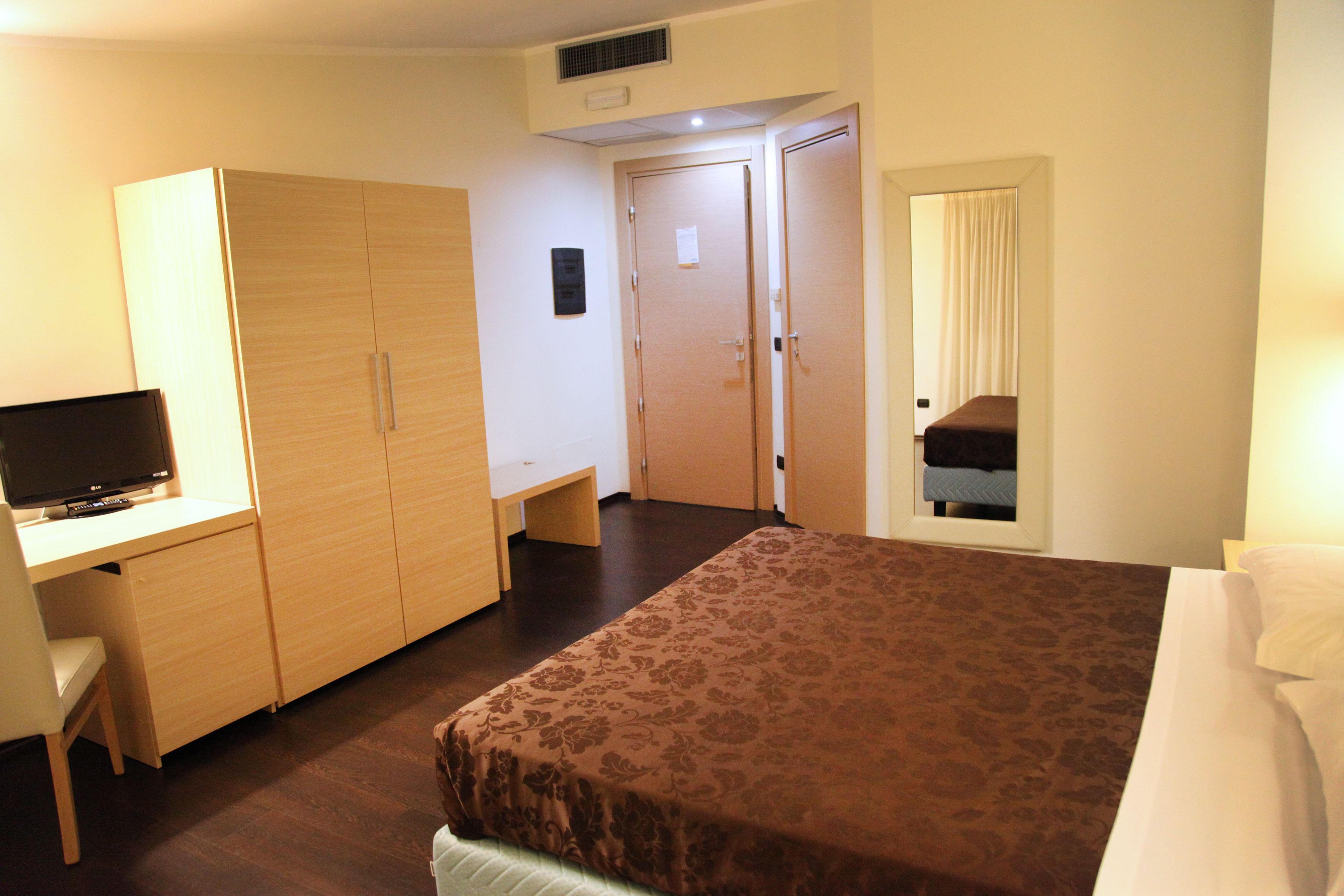 A hotel room with a bed, a desk with a TV, a wardrobe, and a bathroom visible through a door.