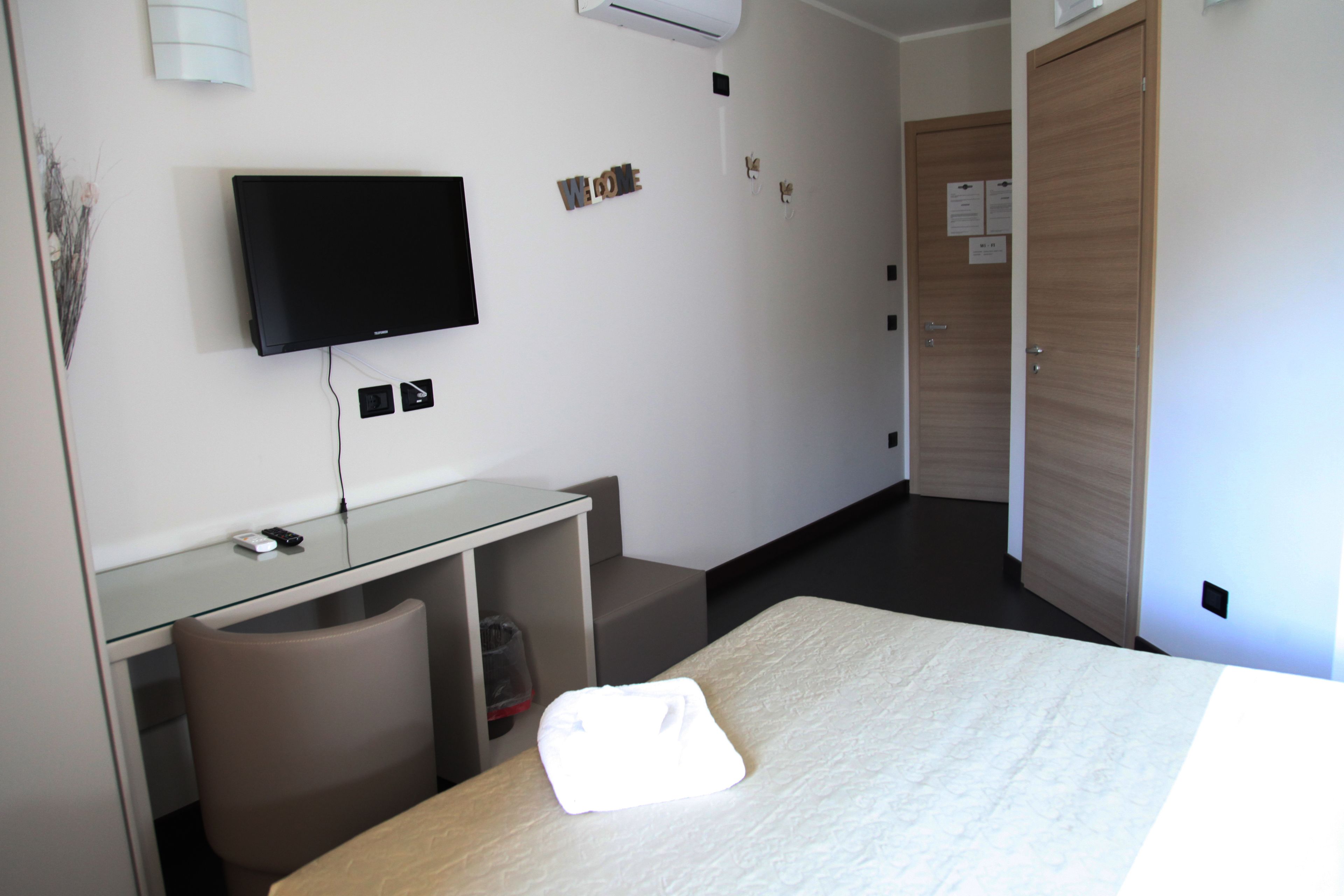 Ein Hotelzimmer mit einem Bett, einem Schreibtisch mit Computer, einem Stuhl, einem an der Wand befestigten Fernseher und einer Tür mit einem Schild.