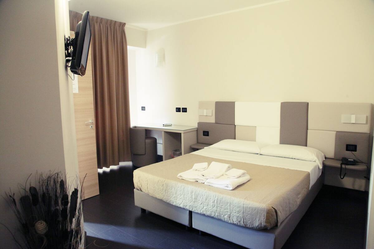 Una habitación de hotel con cama, escritorio y televisor montado en la pared.