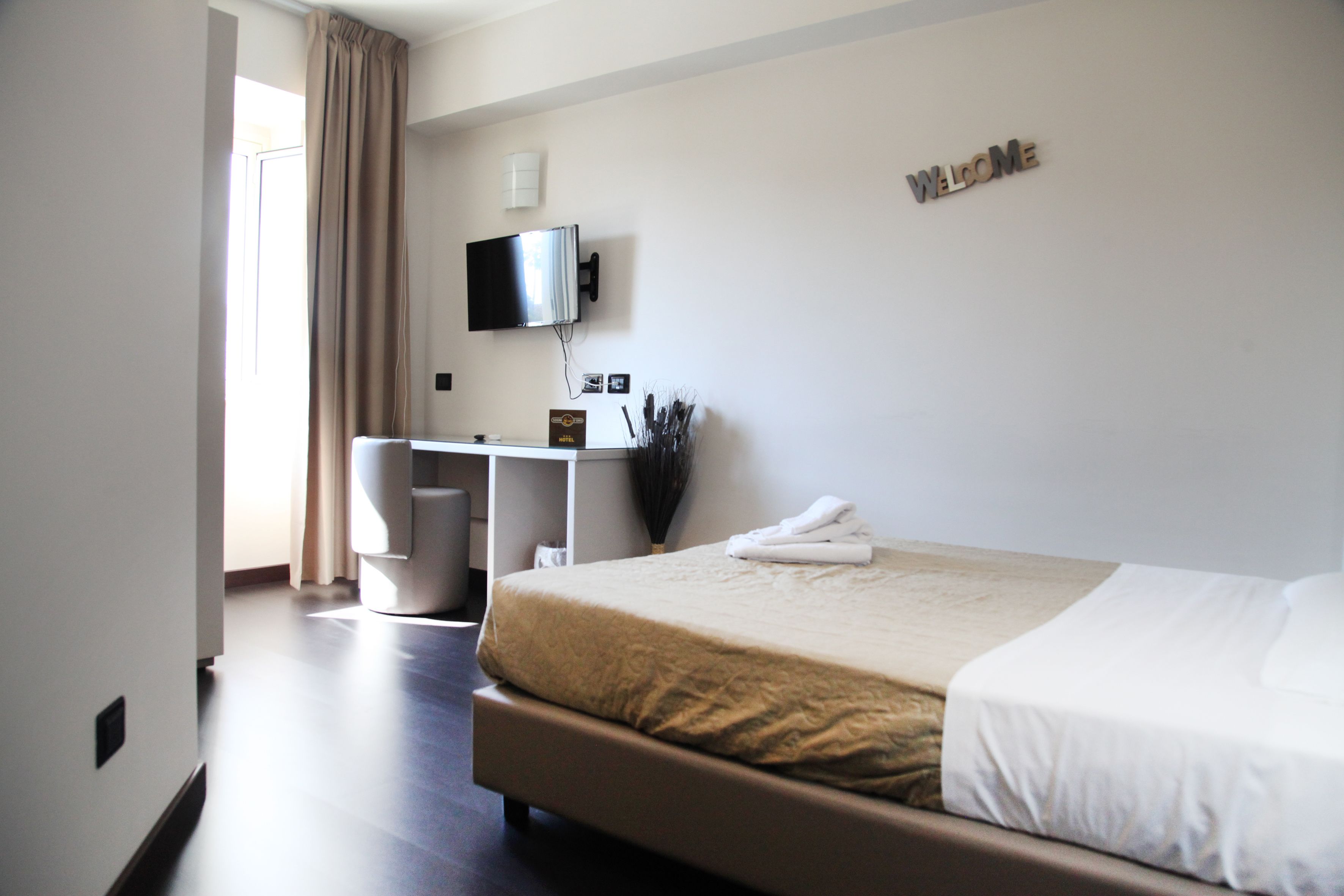 Une chambre d’hôtel avec un lit, un bureau, une télévision et une pancarte « BIENVENUE » accrochée au mur.