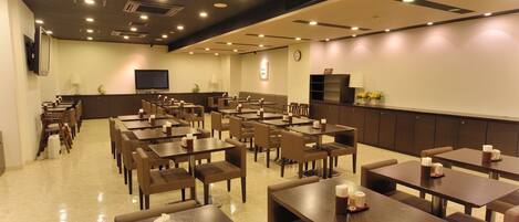 Un restaurante amplio con varias mesas y sillas, un televisor de pantalla plana y un reloj en la pared.