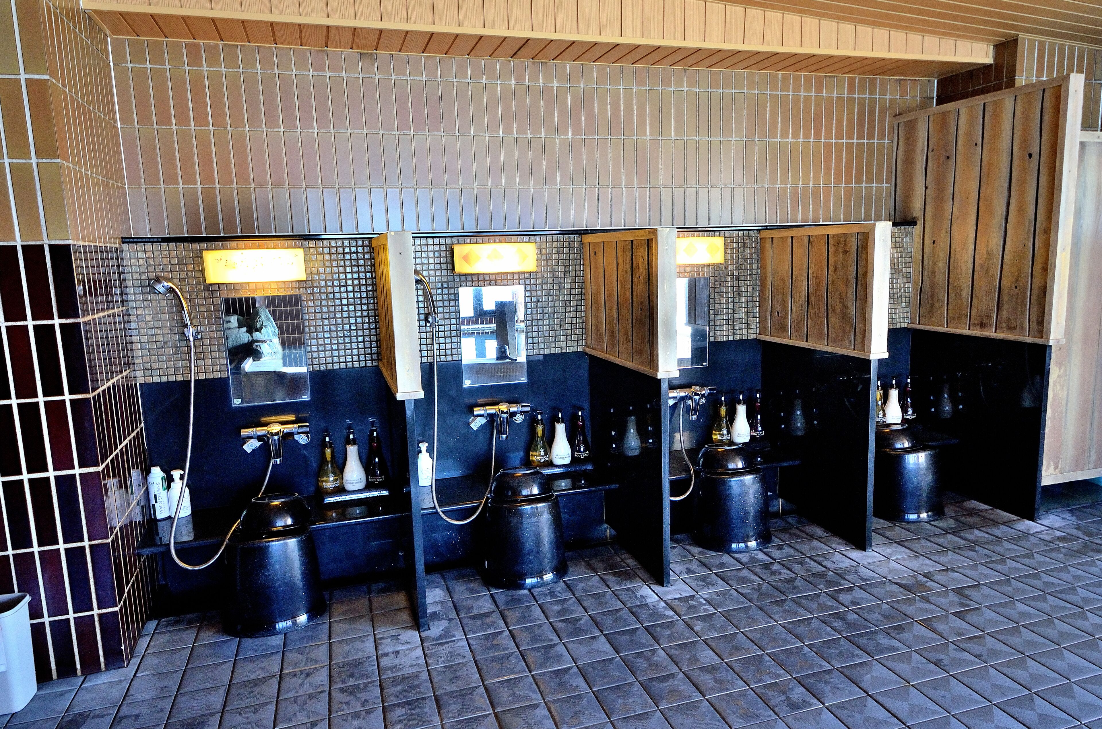 Baño público con varios lavamanos, espejos y contenedores negros para basura.