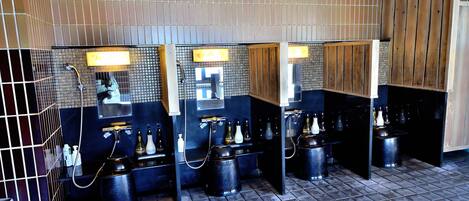 Baño público con varios lavamanos, espejos y contenedores negros para basura.