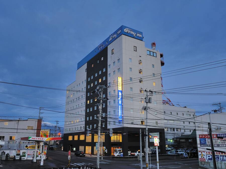 A multi-story hotel with a prominent blue sign on the top, multiple windows, and a visible entrance area with a parking lot.
