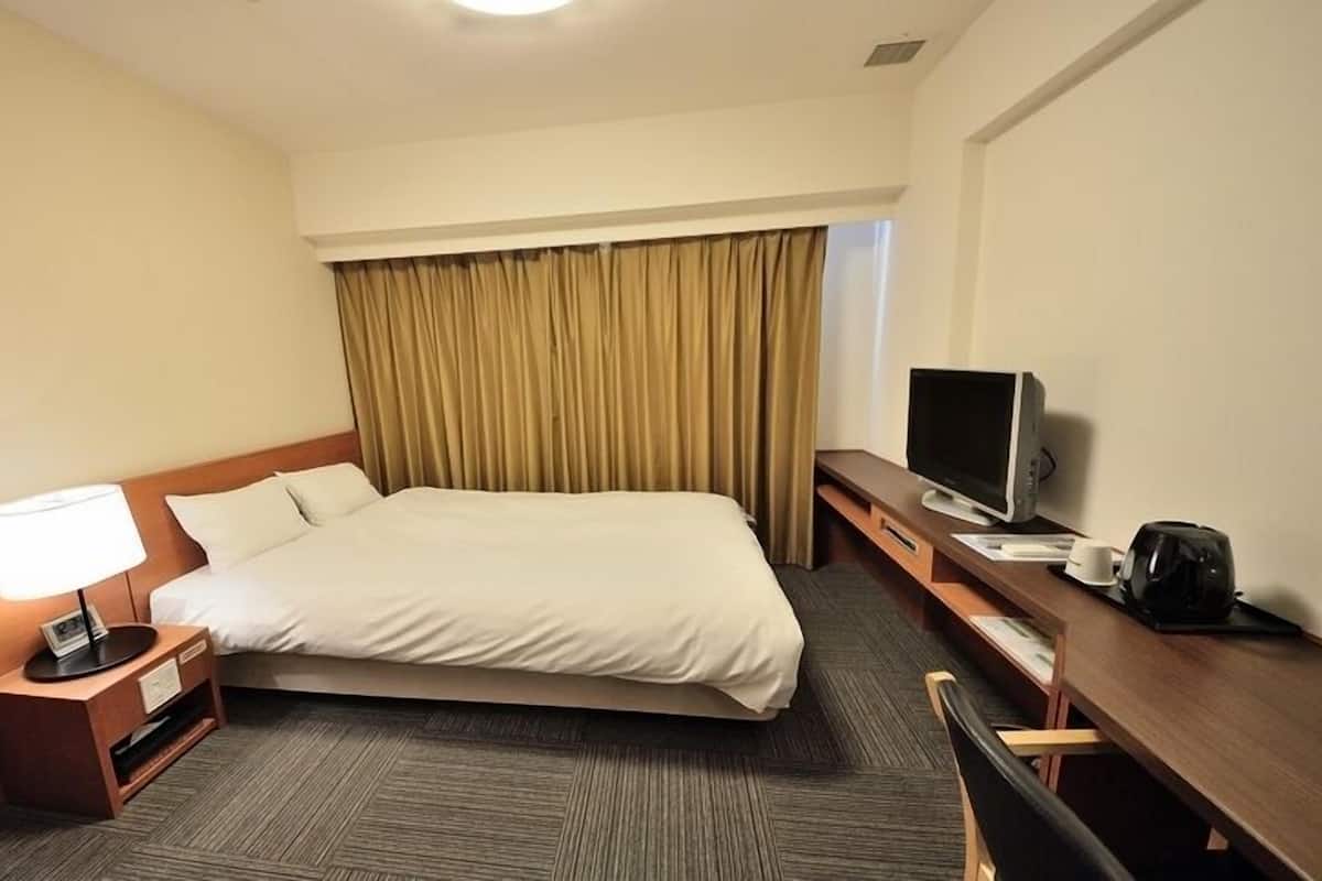 A hotel room with a bed, a desk with a TV, a lamp, and a coffee maker.