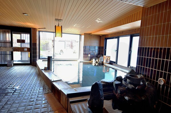 A traditional Japanese onsen with a wooden interior, a tiled floor, and a stone seating area by the pool. - Dormy Inn Hirosaki Natural Hot Spring (Hirosaki)