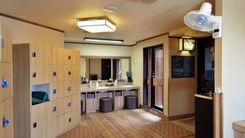 A hotel room with wooden lockers, a sink, a mirror, a fan, and a door with a sign.