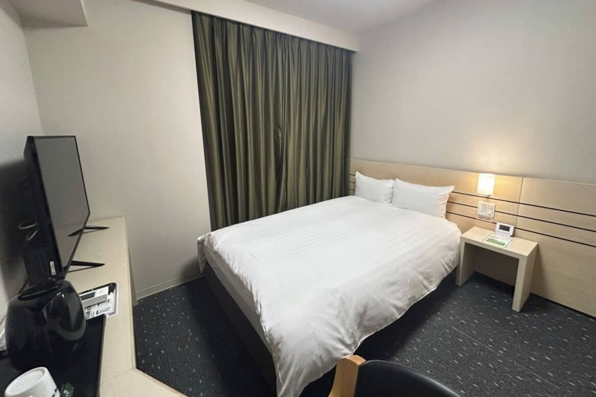 Ett hotellrum med en säng, ett skrivbord med en lampa, en tv och en kaffebryggare.
