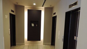 A hallway with two elevators, a door with a sign, and a tiled floor. - Dormy Inn Akita Natural Hot Spring (Akita)
