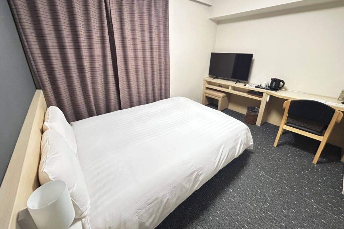 Ett hotellrum med en säng, ett skrivbord med en tv, en stol och en kaffebryggare.