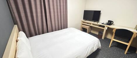 A hotel room with a bed, a desk with a television, a chair, and a coffee maker.