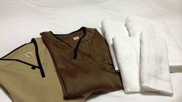 A neatly made bed with a white sheet and two folded shirts in olive and brown colors.
