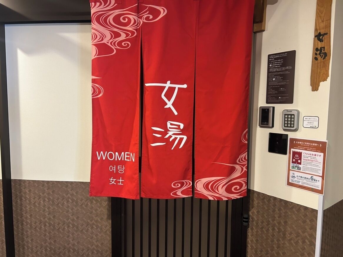 A red banner with 'WOMEN' and '여행여성' text, a wall-mounted information board, and a wooden panel.