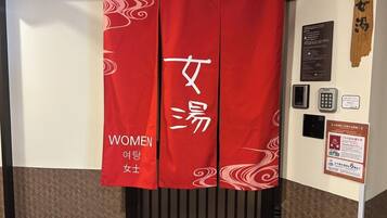 A red banner with 'WOMEN' and '여행여성' text, a wall-mounted information board, and a wooden panel.